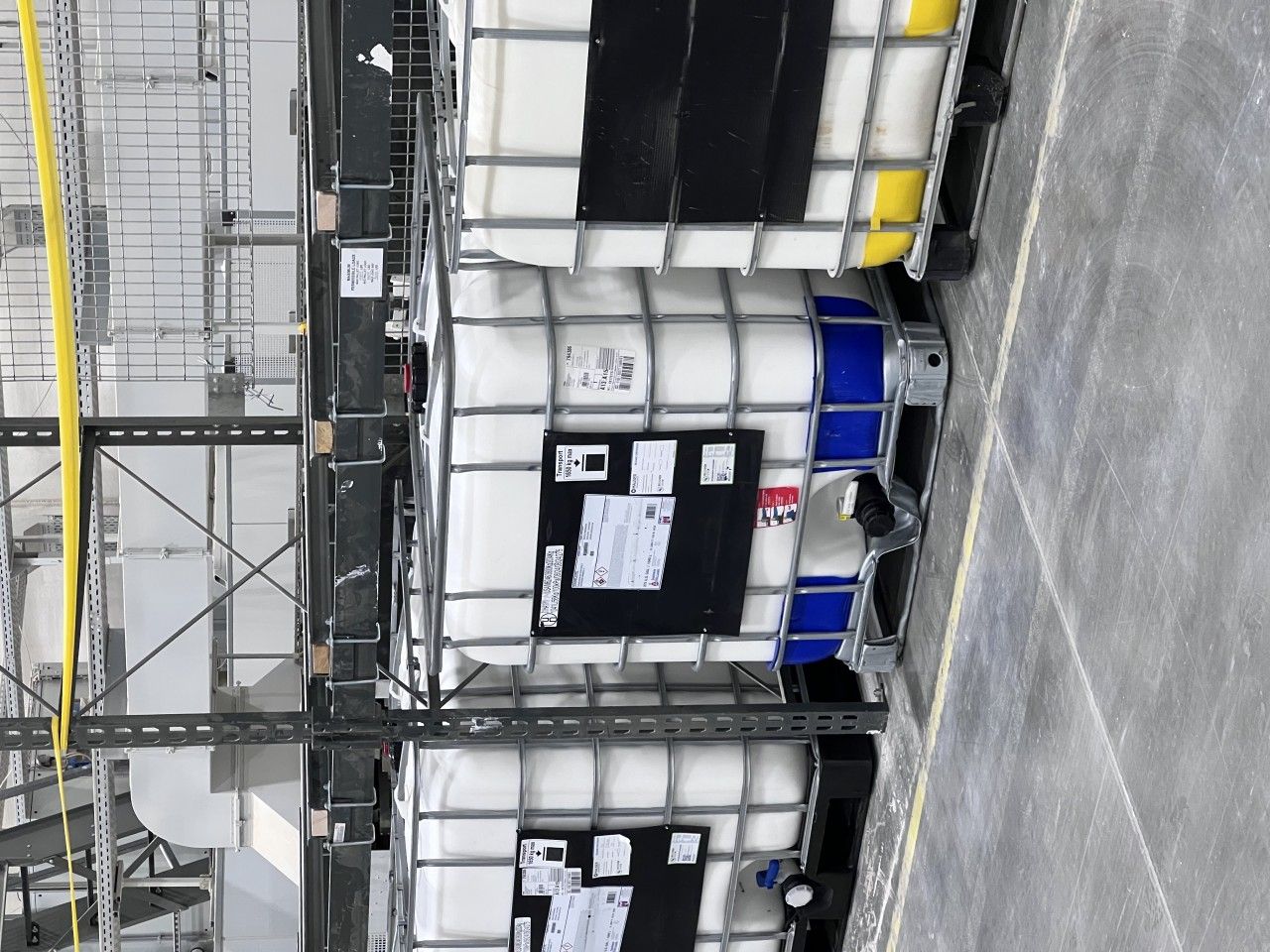 White IBC totes stacked in a warehouse, some with blue and yellow accents.