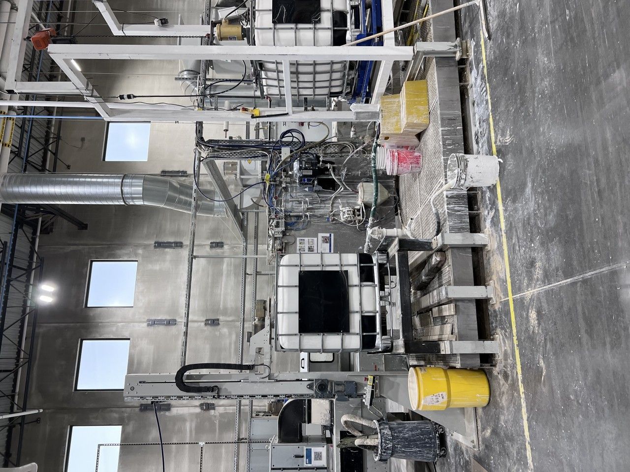 Factory interior with industrial equipment and piping, various tanks, and concrete floors.