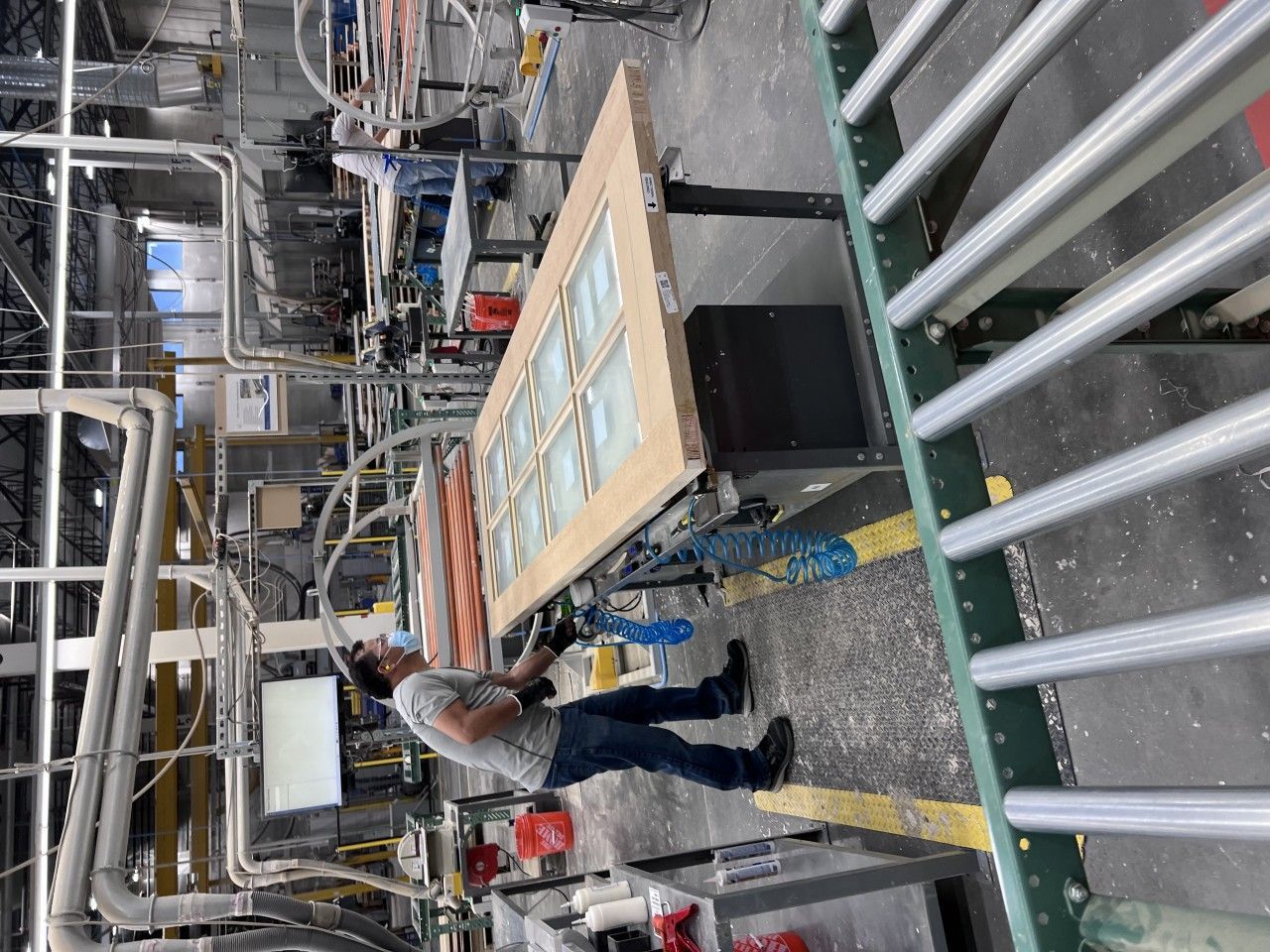 Person working on a door in a factory. They are standing next to a conveyor belt with equipment.