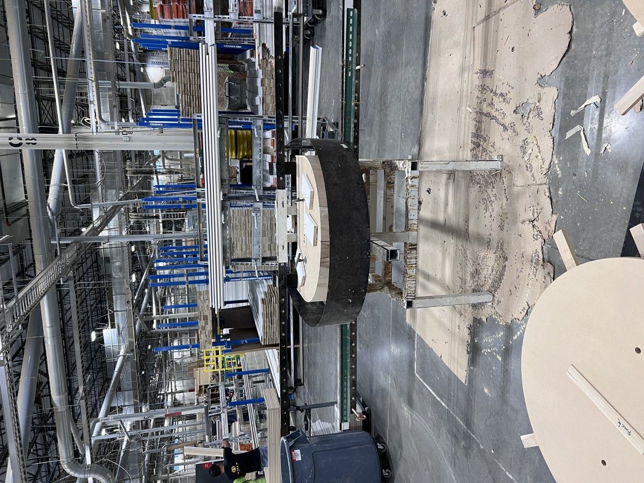 A large wooden spool sits on supports in a factory. Conveyor belts and machinery surround it.