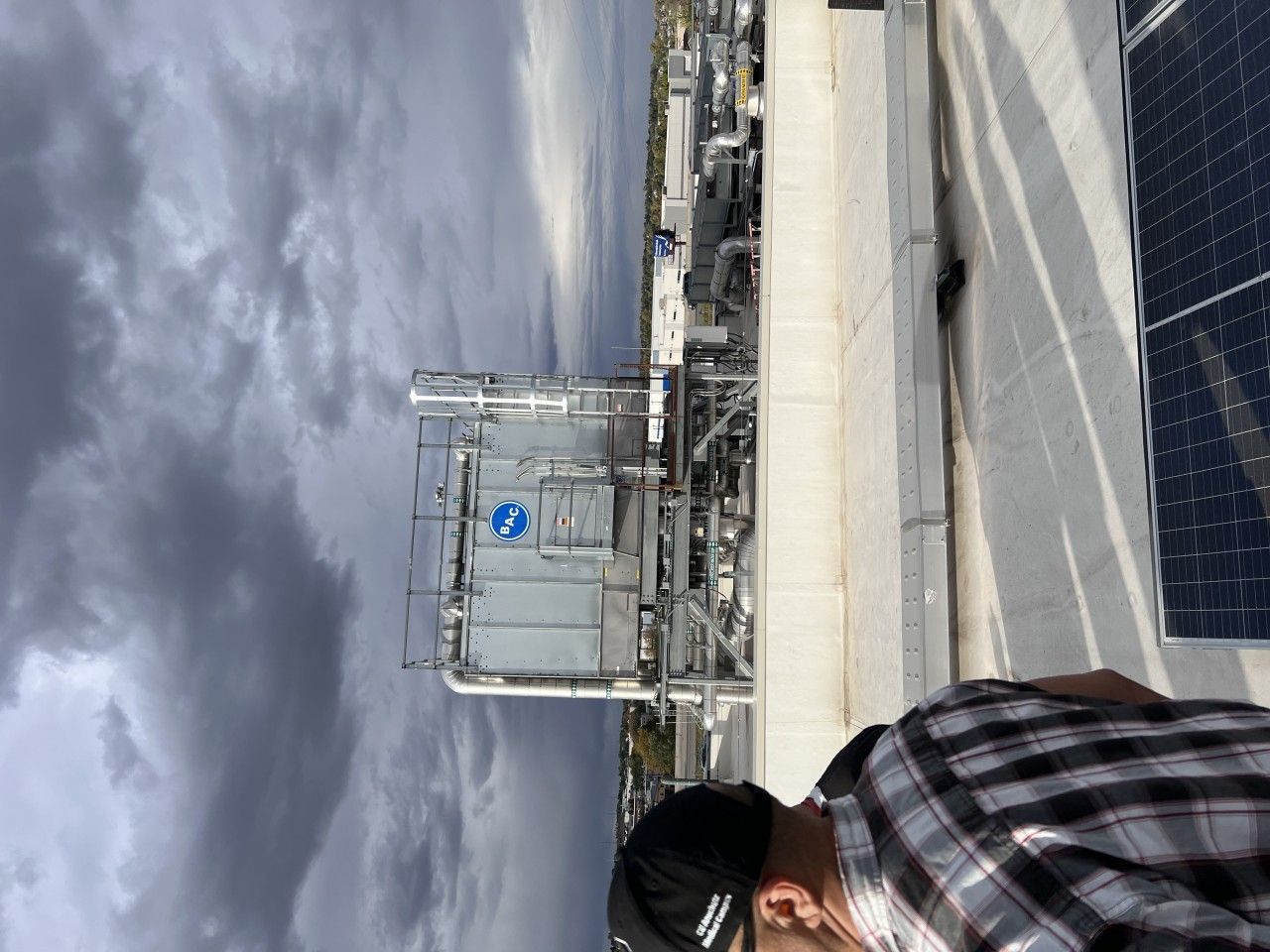 Person near industrial rooftop equipment under cloudy sky.