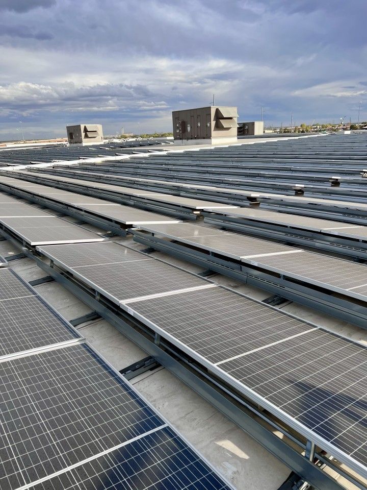 Solar panels installed on a flat roof, with small square structures in the background under a cloudy sky.