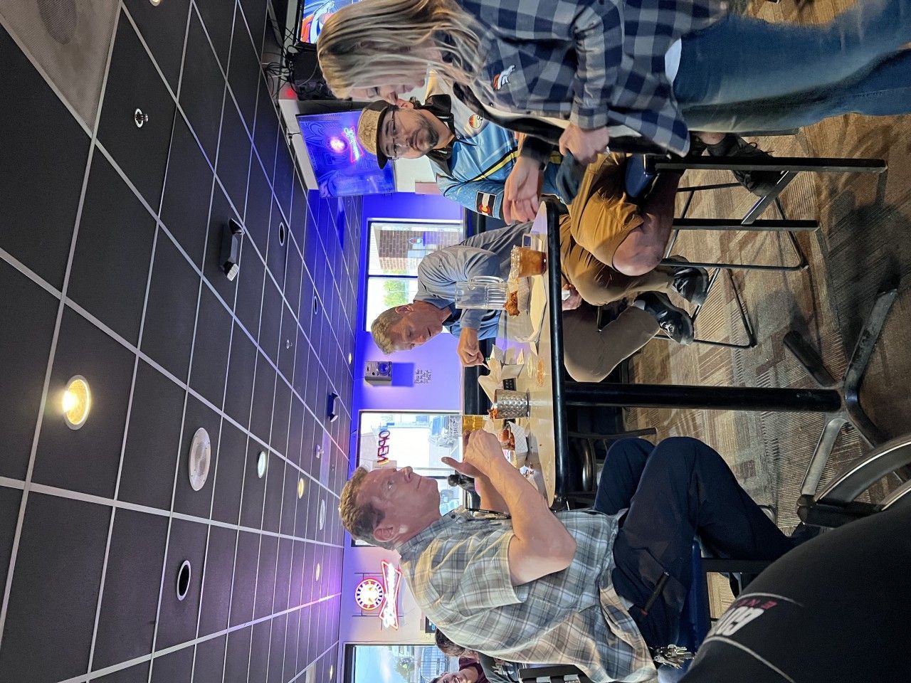 People at a table in a bar, looking at something. Black tile wall.