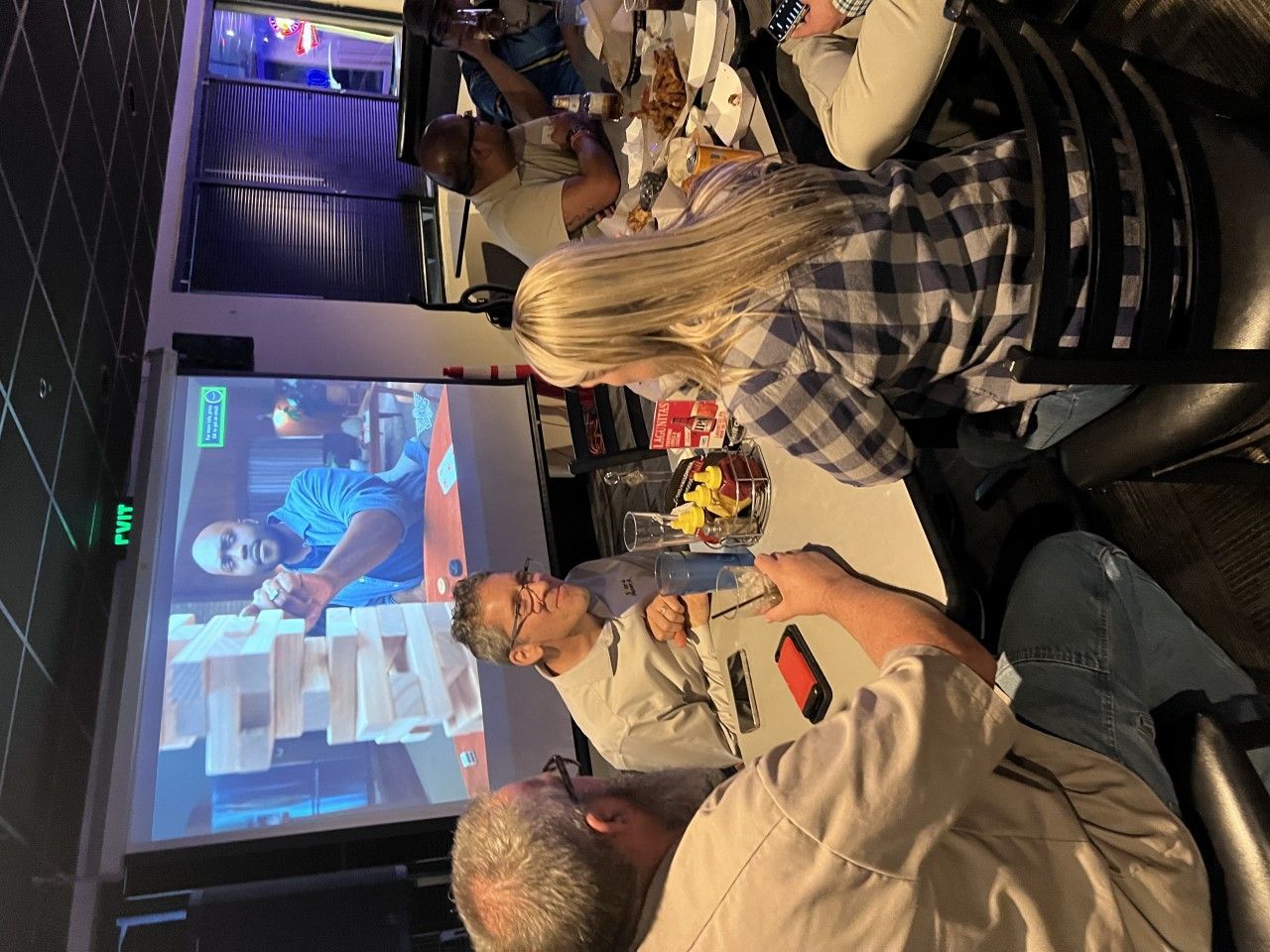 People at a table watching a video of someone playing Jenga, with food and drinks present.