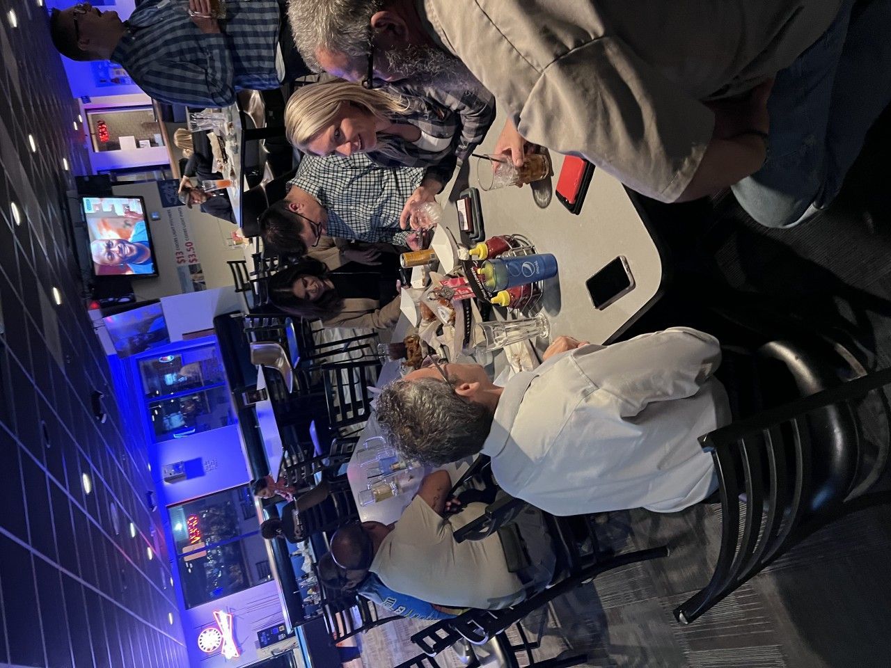 People gathered at tables in a bar, some eating, talking, and looking at phones.