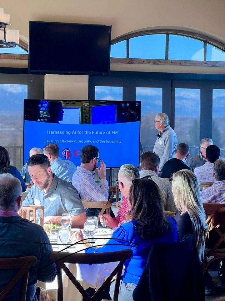 A presentation on AI in a dining room. Attendees are seated at tables, listening to a speaker in front of a screen.