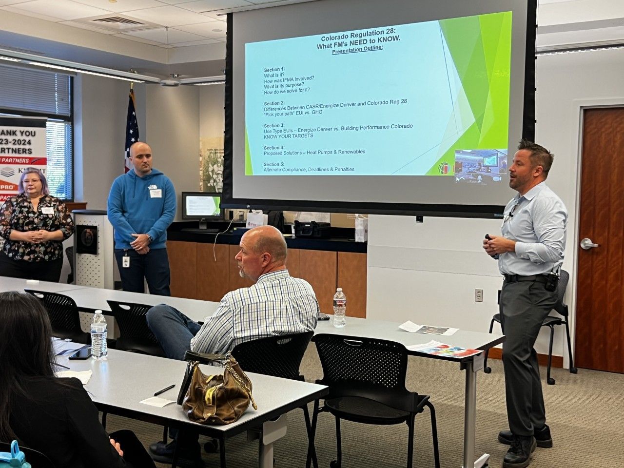 Man presenting to a group in a conference room, screen with notes displayed.