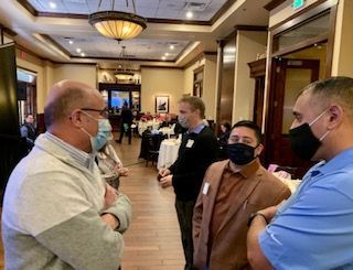 People wearing masks talking in a well-lit interior. Other people and tables are visible in the background.