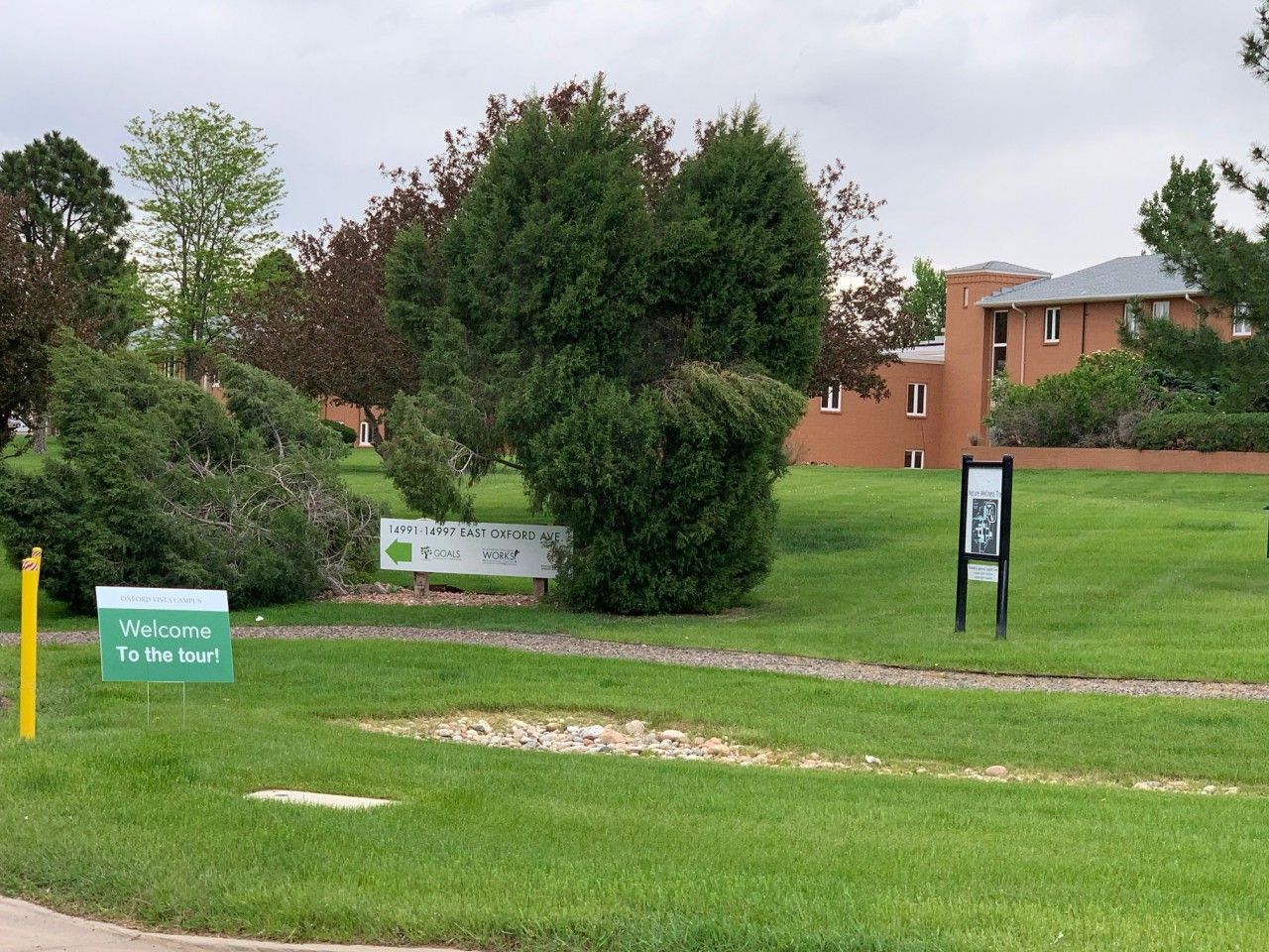 Entrance to a court with green signs and landscaping, a brick building in the background.