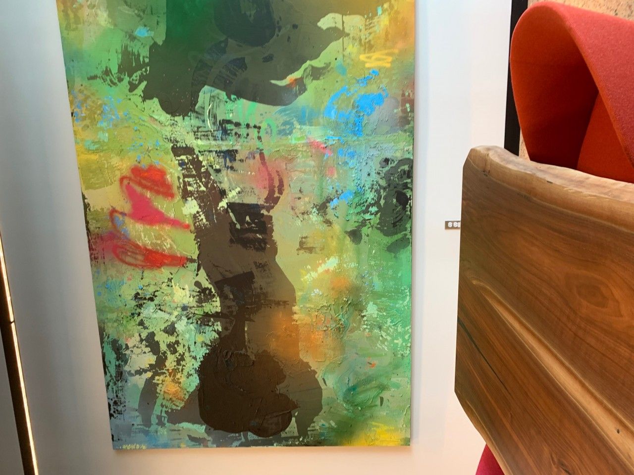 Abstract art in shades of green, blue, brown, and yellow. A wooden chair is on the right.