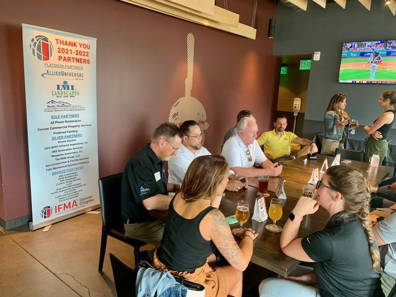 People at a table inside a restaurant. Banner on the left, TV playing baseball game in the background.