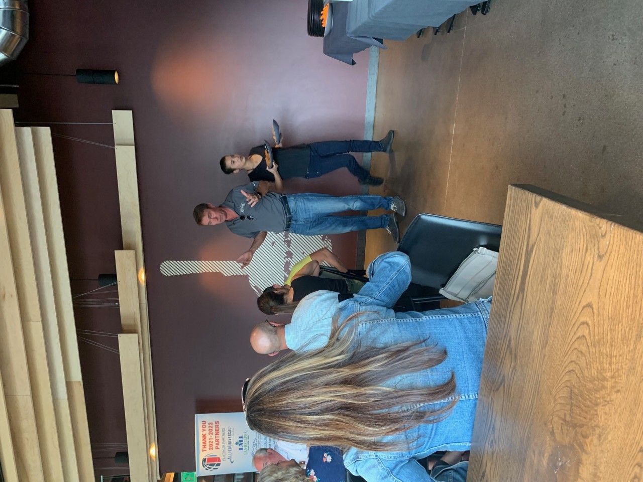 A band performs indoors: two guitarists and a person at a microphone, audience present, warm lighting.