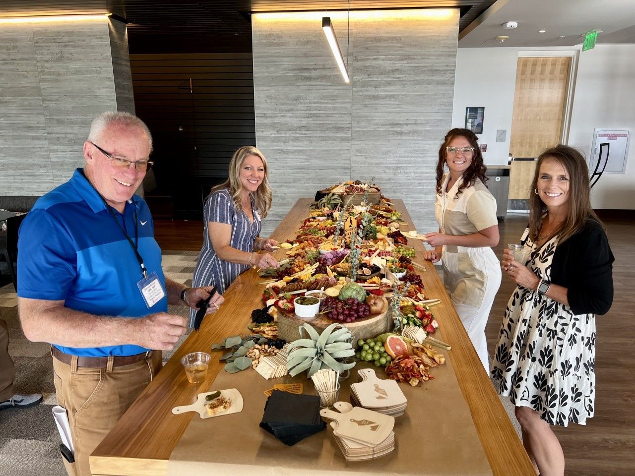 Four people at a long table with charcuterie. Man in blue shirt, women in summer dresses.