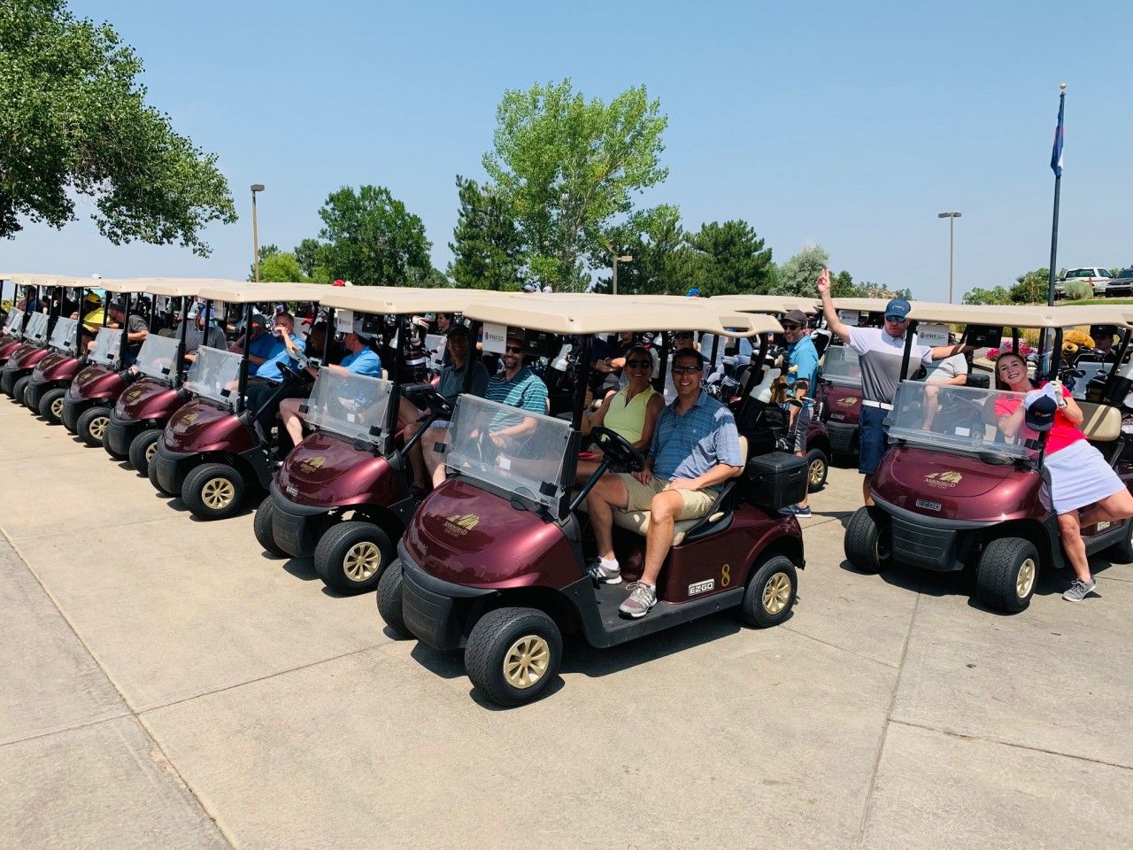 A long line of maroon golf carts with people in them, parked outside on a sunny day.