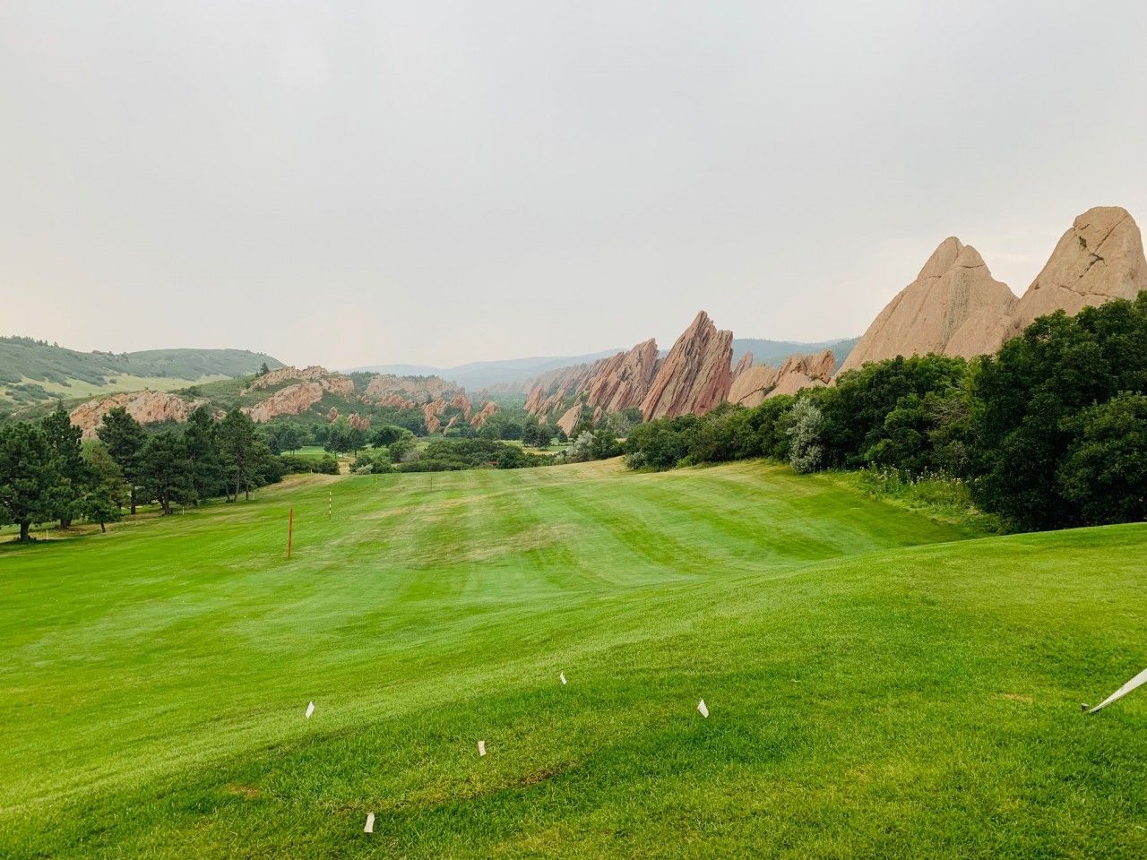 Green golf course with red rock formations in the background under an overcast sky.