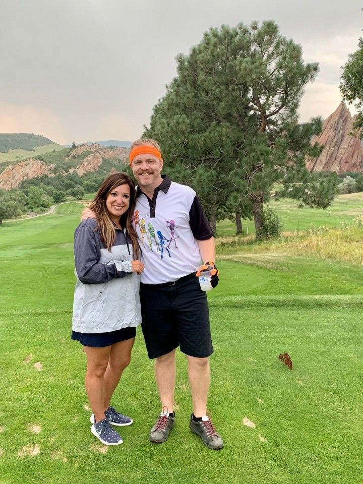 A couple smiles, posing on a golf course.