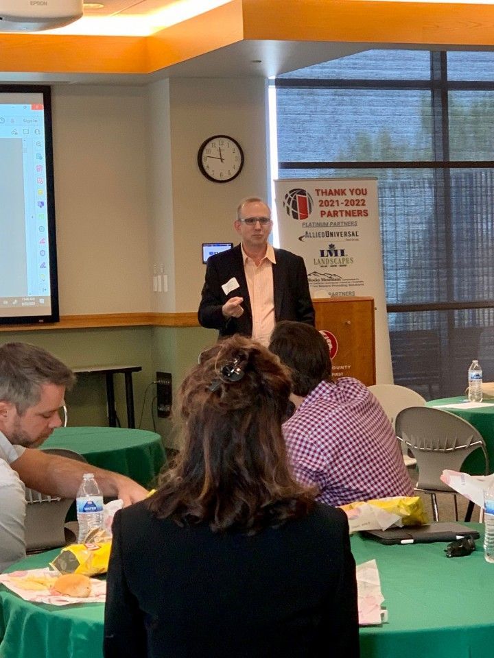 Man in suit giving a presentation to a small group seated at tables.