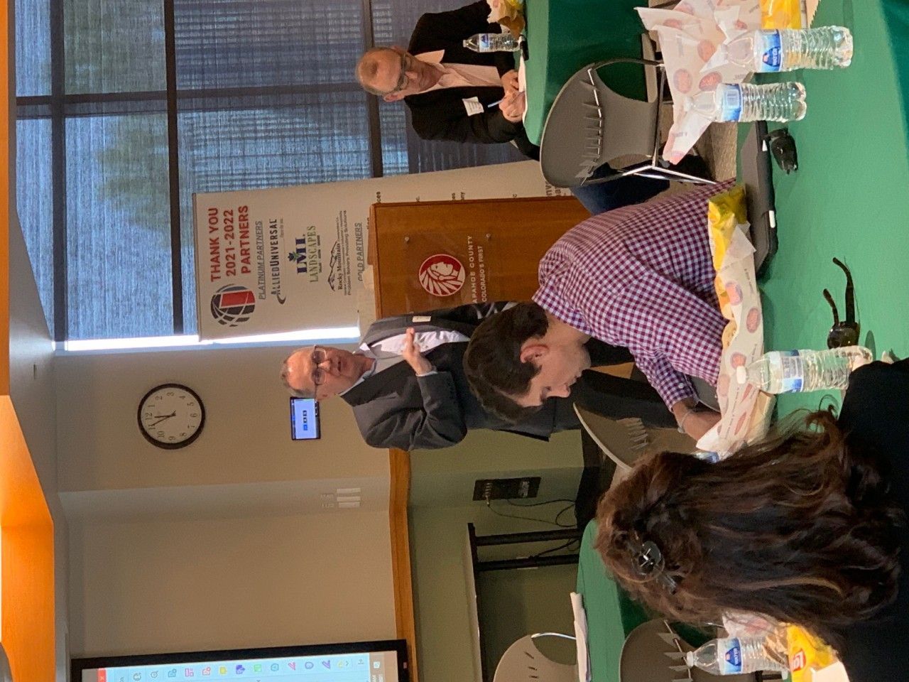 Man speaking at a podium during a presentation, with audience members seated at tables.