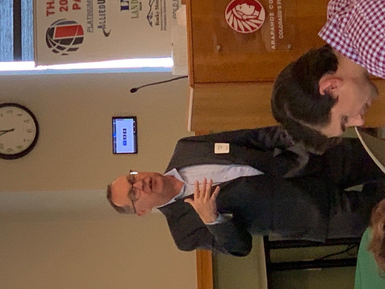 Man in a suit speaks at a podium; audience members.