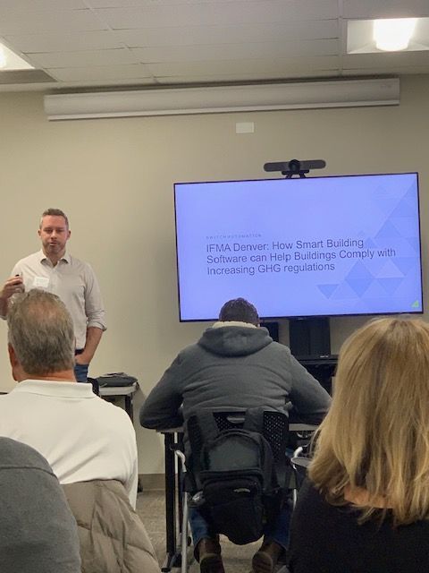 Man presenting a slideshow about smart building software. Audience members include a person in a wheelchair.