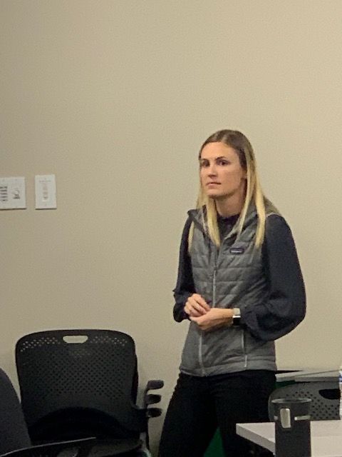 Woman standing in a room, wearing a vest and looking to the side.