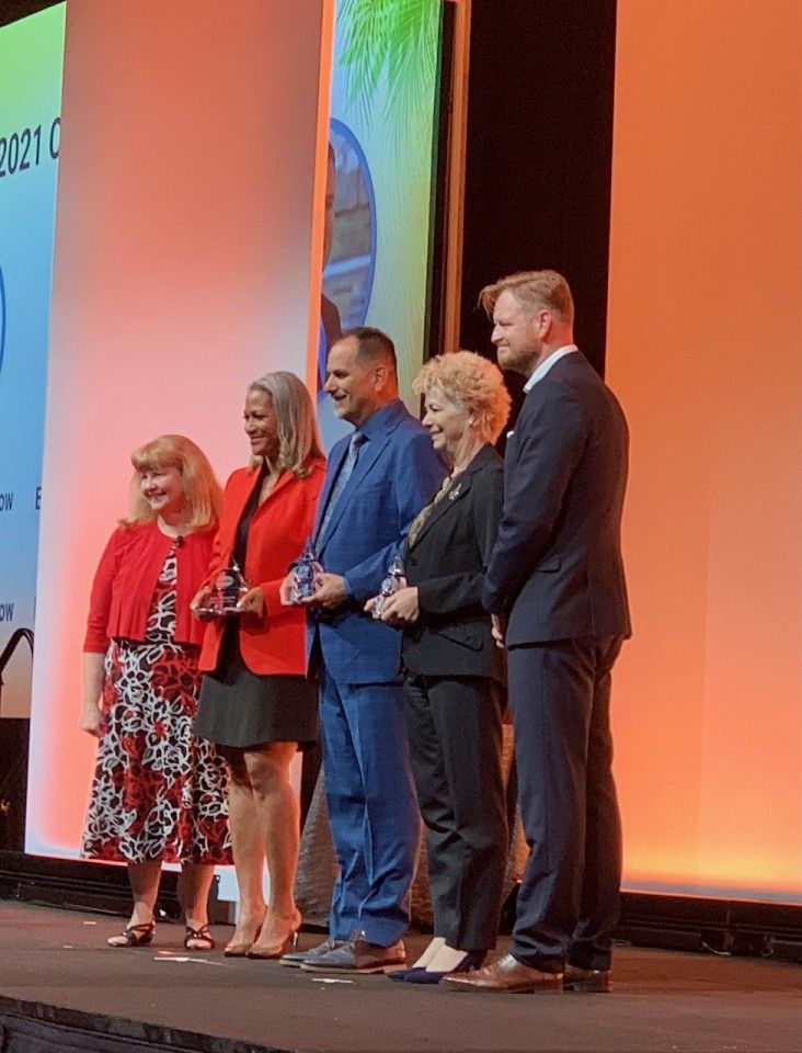 People on stage holding awards, smiling, in front of a backdrop, at an event.