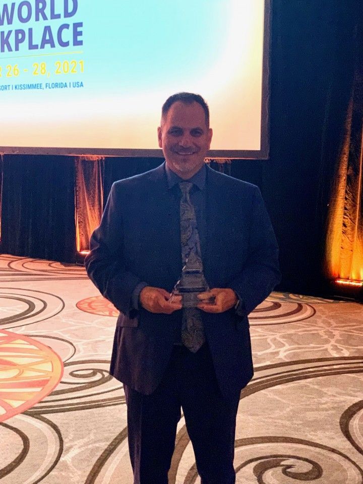 Man in suit holding an award, standing in front of a conference backdrop.