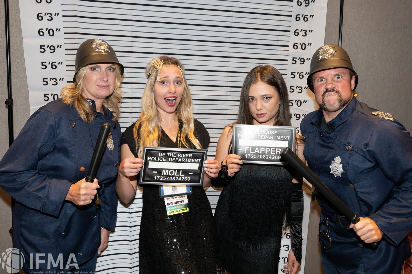 Four people in police costumes pose for a mugshot.