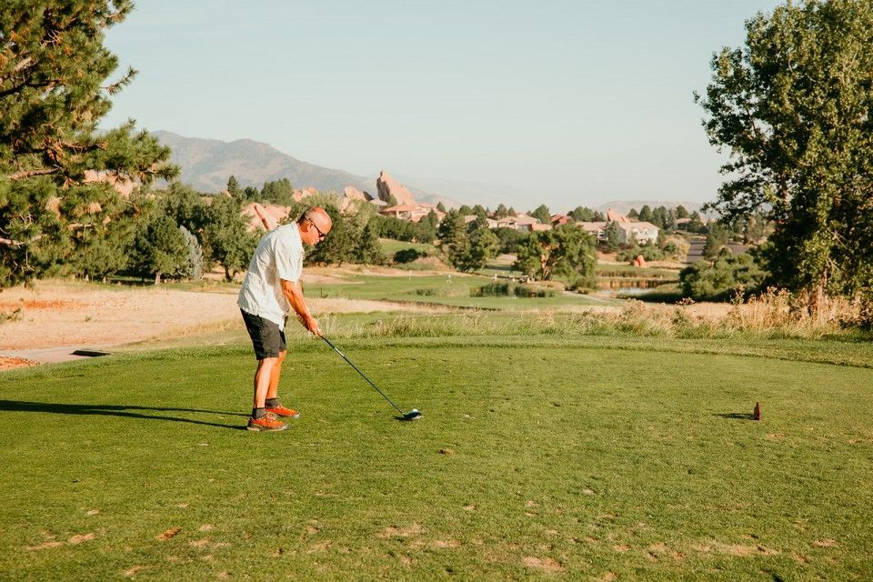 Man teeing off on a golf course with mountains in the background.