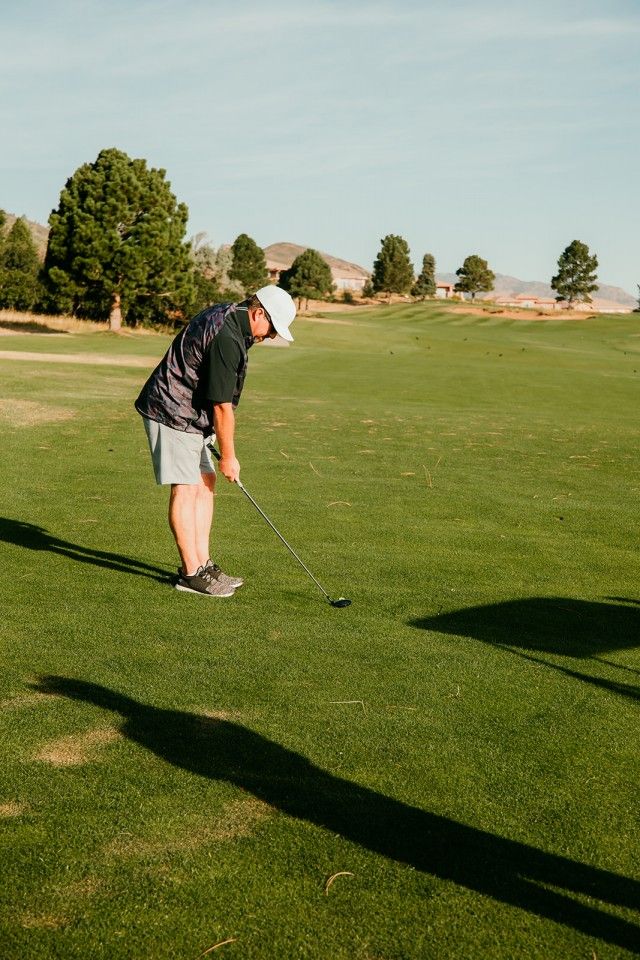 Man putting on a green golf course, wearing a hat and vest.