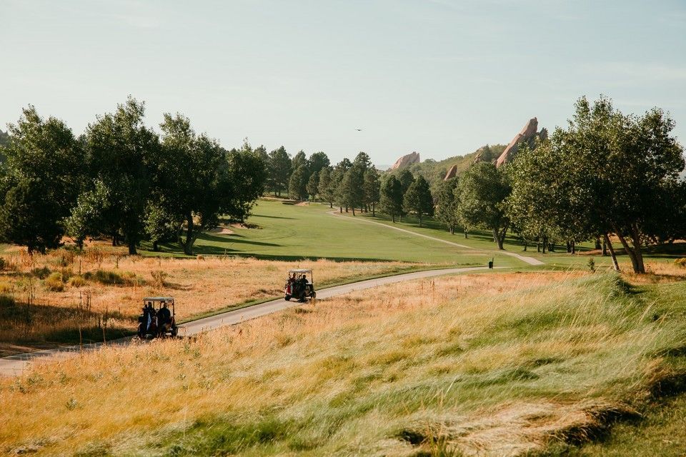 Golf course scene with golf carts on a path, trees and golden grasses.