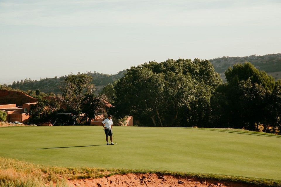 Golfer on green, putting. Sunny day with trees and hills in the background.