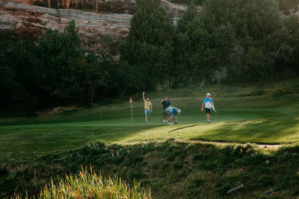Golfers celebrating on a green. Trees and a red flag in the background. Sunny day.
