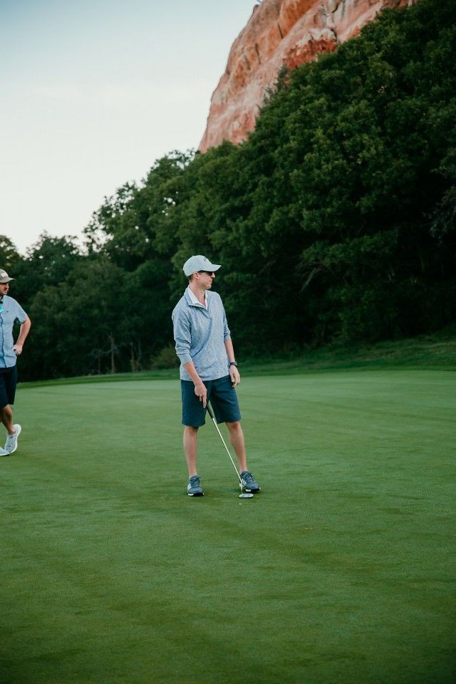 Man putting golf ball on green with scenic backdrop.