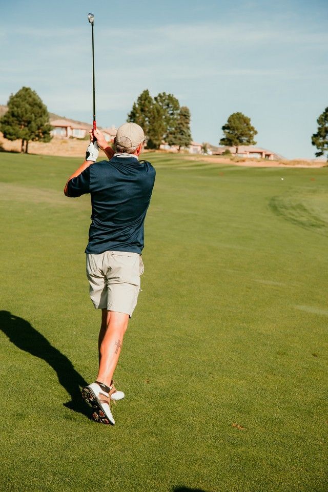 Golfer swinging a club on a green field under a clear blue sky.