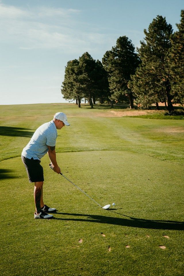 Man on a golf course about to swing. Green grass, blue sky, trees in the background.
