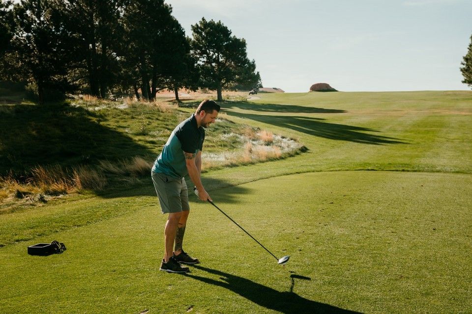 Man on golf course preparing to swing; green grass, sunny day.
