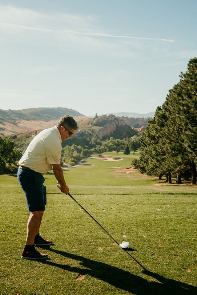 Golfer teeing off on a sunny course with a mountain backdrop.