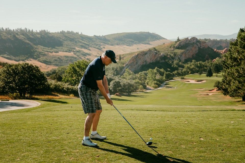 Golfer teeing off on a green, mountains in the background. Sunny day.