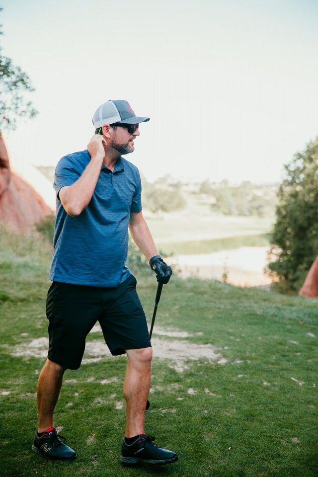 Man in golf attire on a course, looking off to the side, holding a golf club.