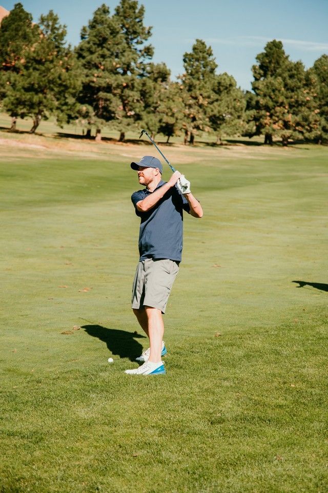 Man in blue shirt swings golf club on green course.