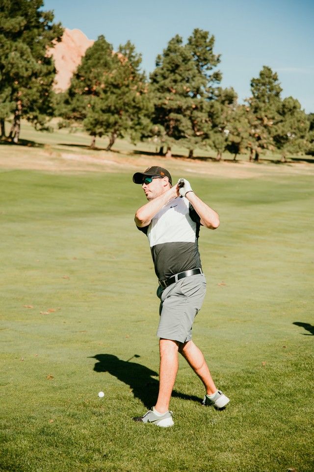 Man swinging a golf club on a green golf course under a clear sky.
