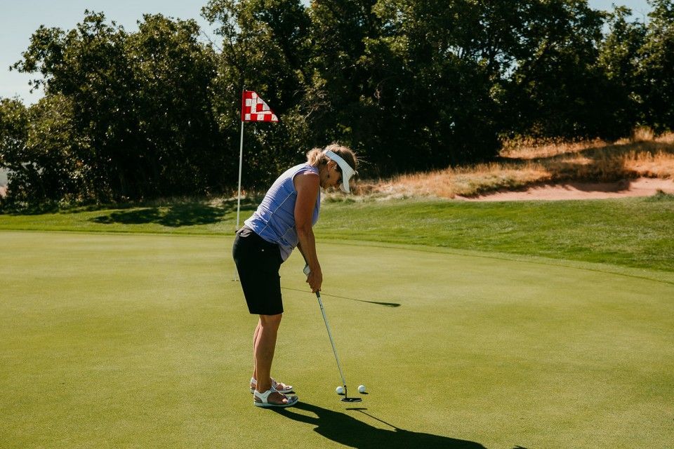 Woman putting a golf ball on a green, flag in background.