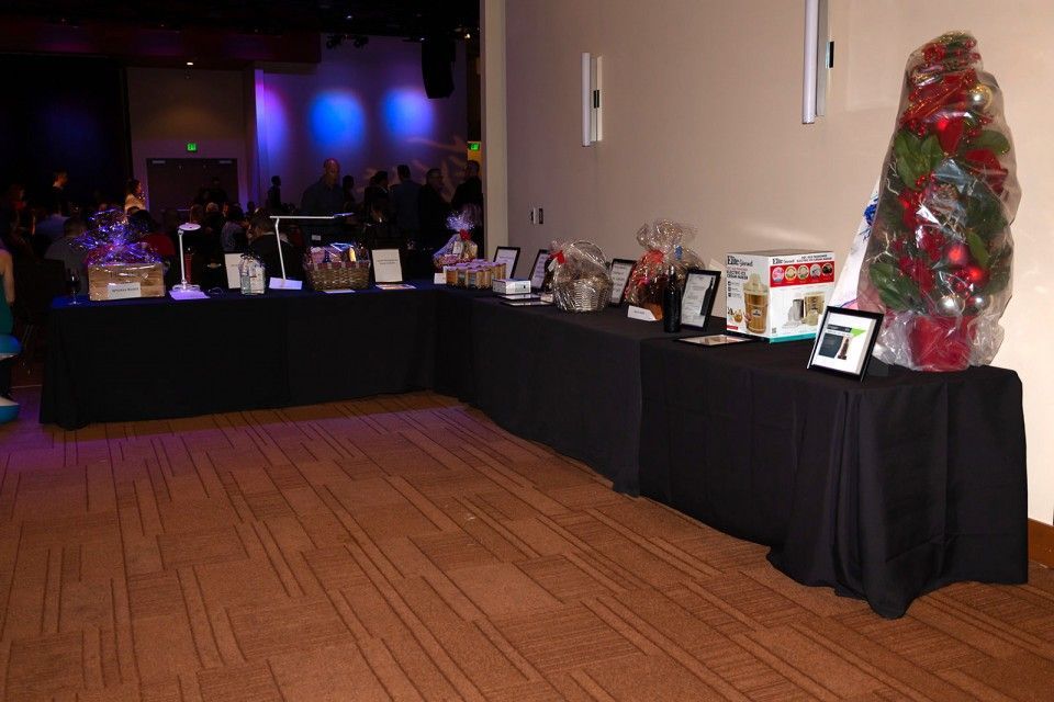 Tables with items on display in a room, likely an event or fundraiser. Black tablecloths and a large decorated tree.