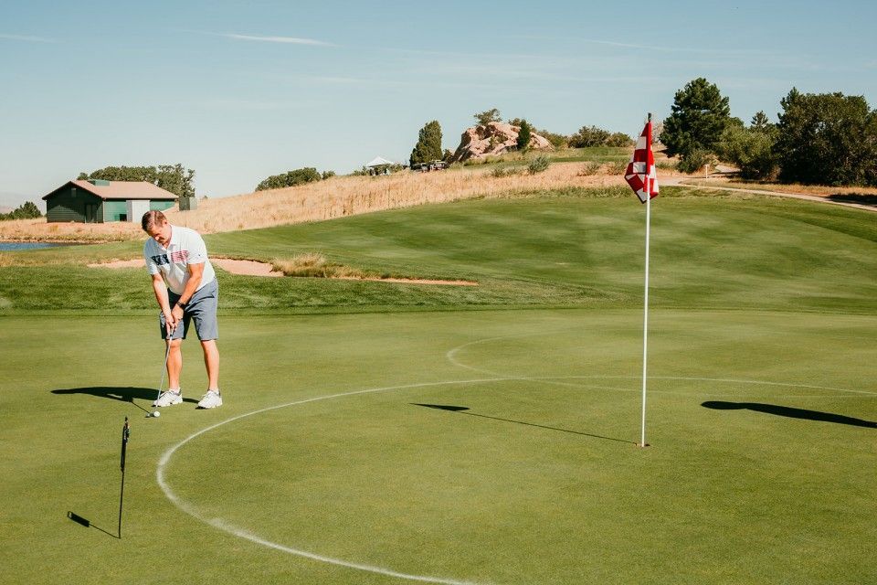 Man putting golf ball on a green with flag, sunny day.