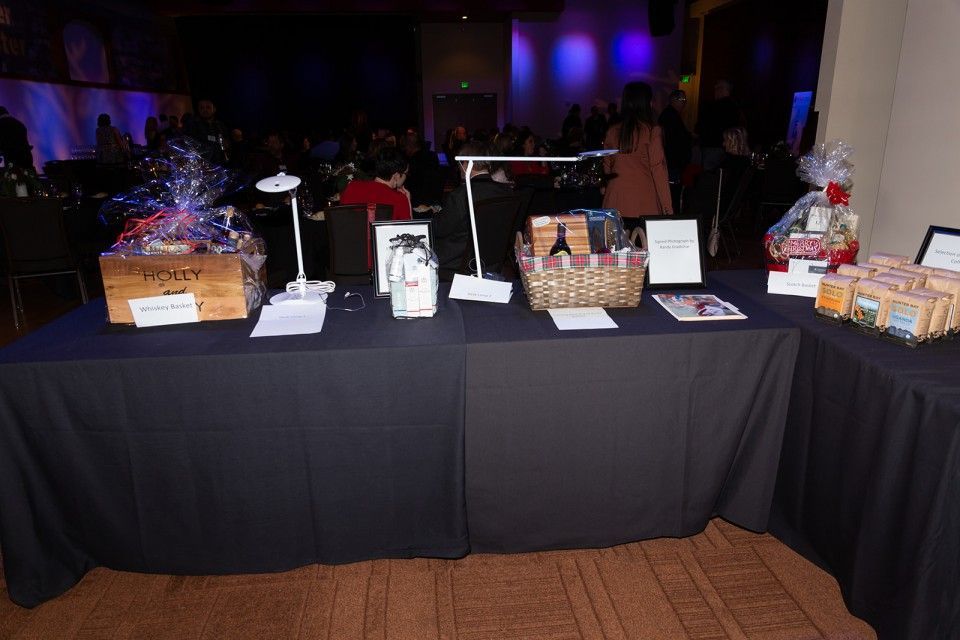Table with baskets and items, possibly for a silent auction, with dark tablecloth and people in the background.