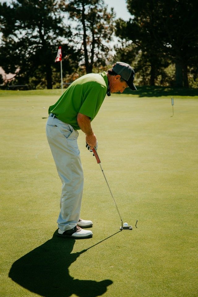 Man in green shirt putting golf ball on a green, sunny day.
