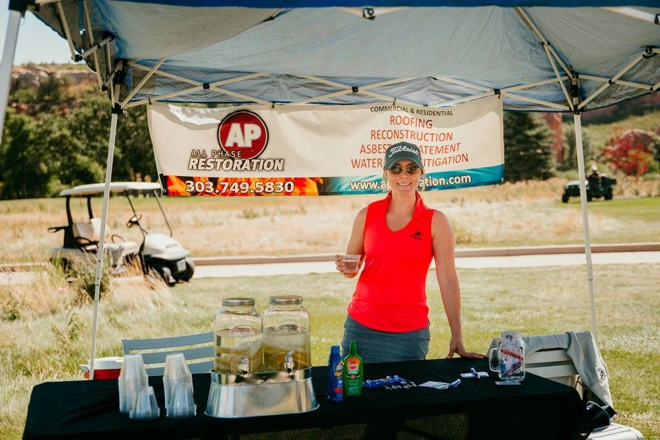 Woman at a refreshment stand, holding a drink, under a tent on a golf course.