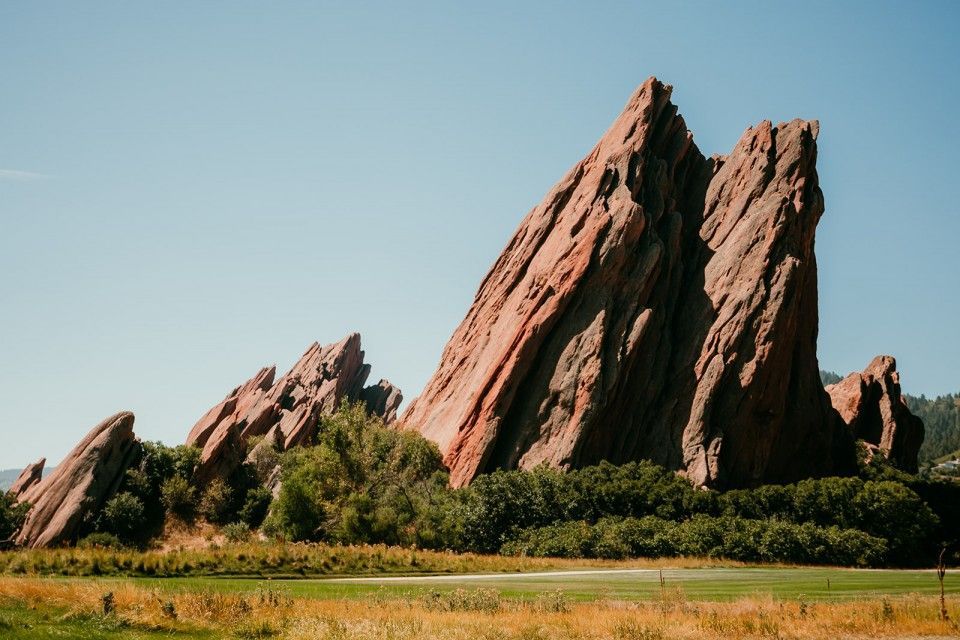 Red sandstone rock formations against a blue sky, with greenery in the foreground.