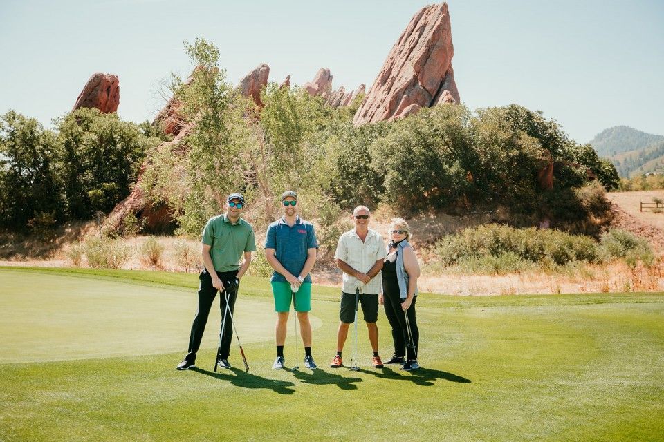 Four people on a golf course with red rock formations in the background. Golf clubs and sunny day.